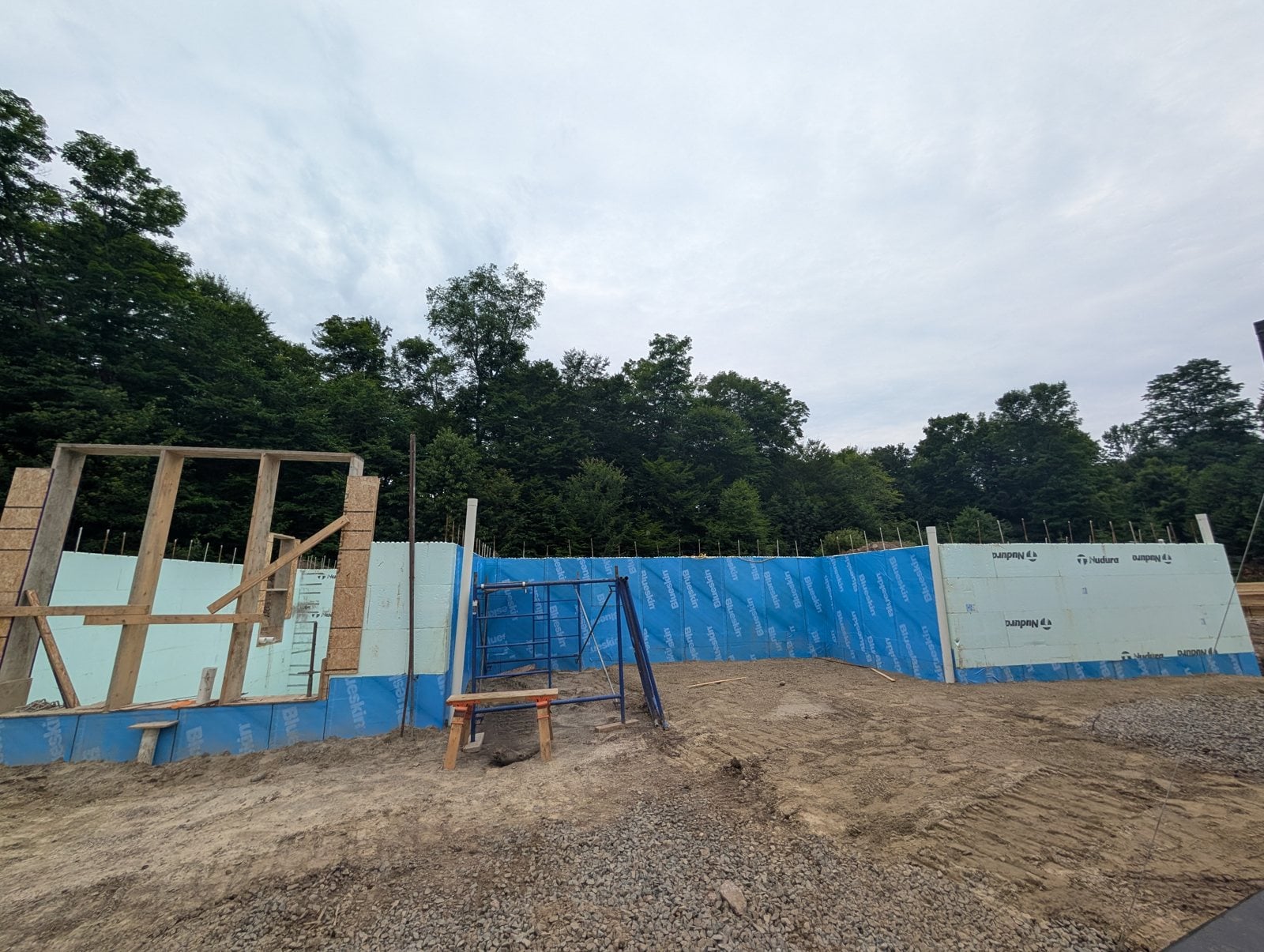 Début du chantier : murs en blocs isolants entourés d'une membrane bleue, avec le cadre d'une ouverture