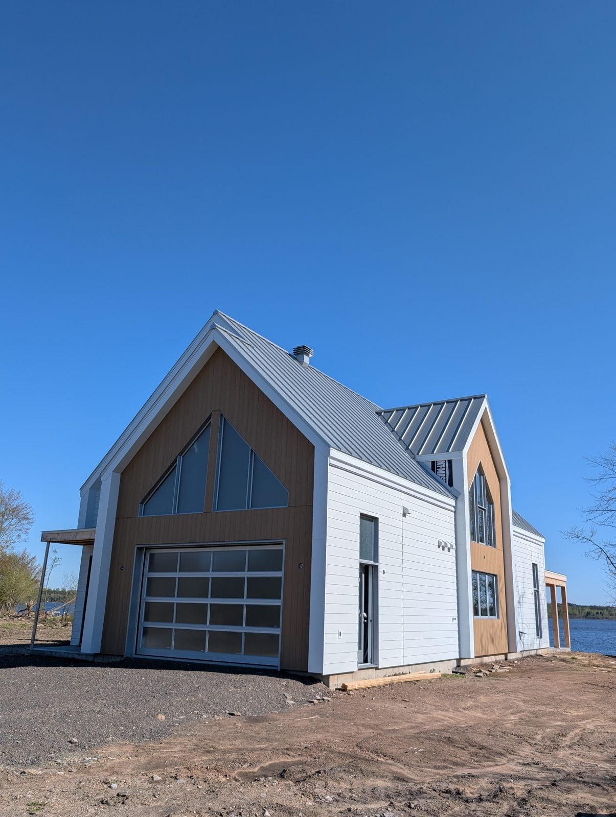 Photo de la maison construite vue de côté, avec son revêtement blanc et sa toiture de tôle