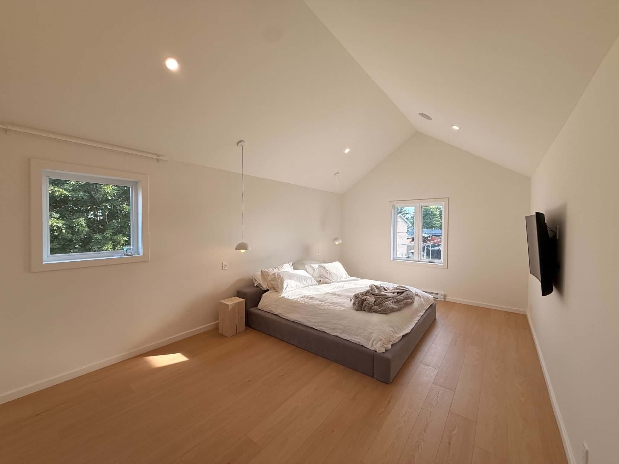 After the work: bedroom under a cathedral ceiling, light wood floor and pendant lights