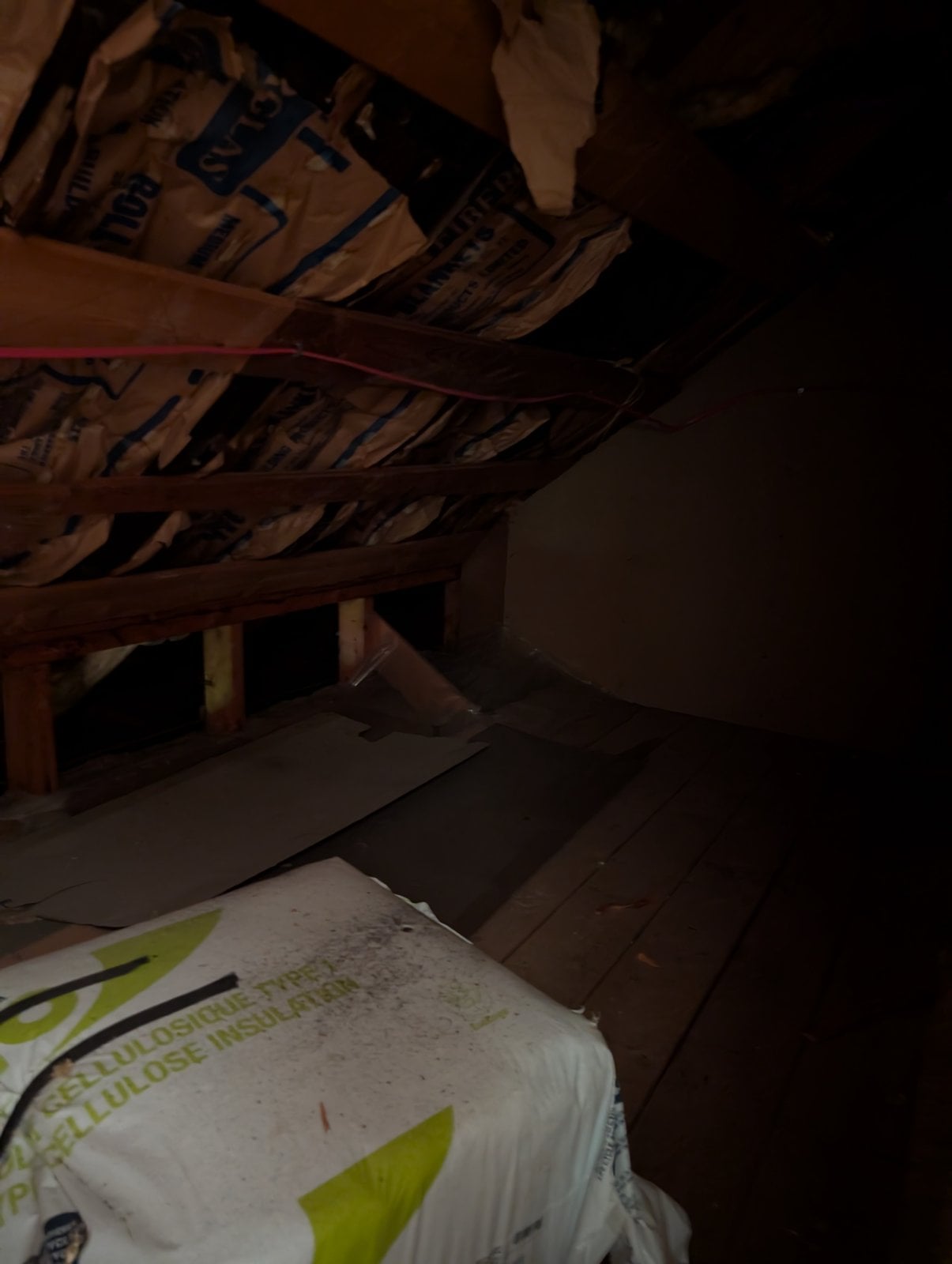 Attic before the work: kraft-paper batt insulation and a bag of cellulose insulation