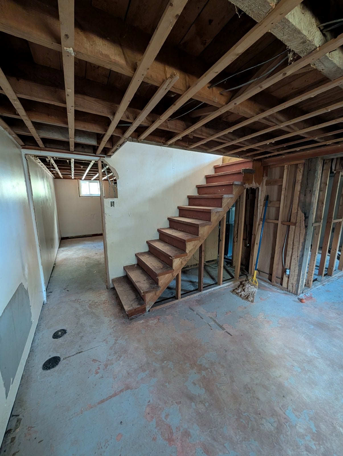 Basement staircase before the work, with stripped walls and a concrete floor