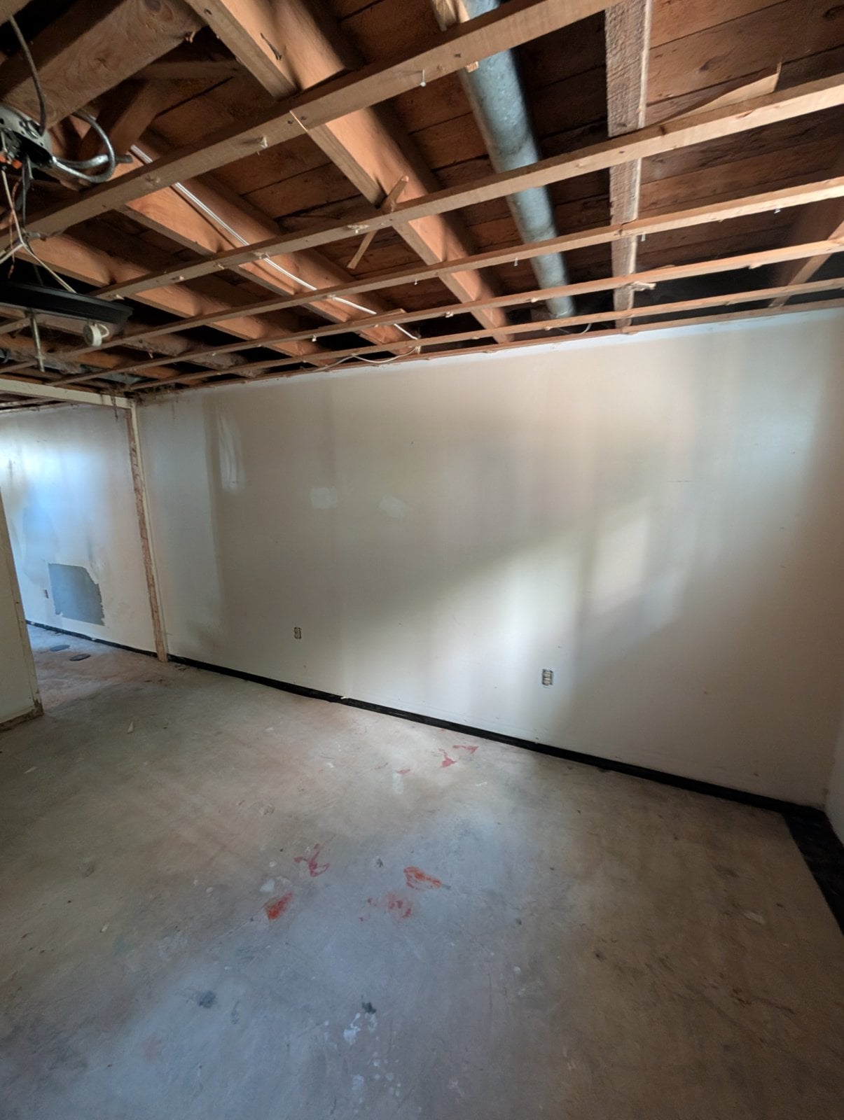 Long basement wall before the work, under an exposed-joist ceiling