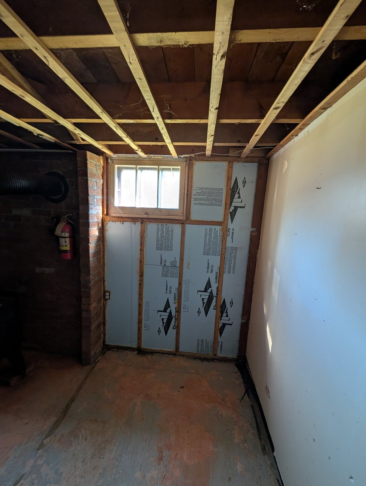 Basement wall insulated with rigid foam, with a small window, before the work